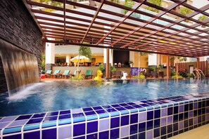 An indoor swimming pool with a tiled edge, a waterfall feature, and lounge chairs. - Andakira Hotel (Patong)