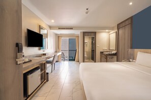 A hotel room with a bed, desk, chair, television, and a bathroom with a shower. - Andakira Hotel (Patong)