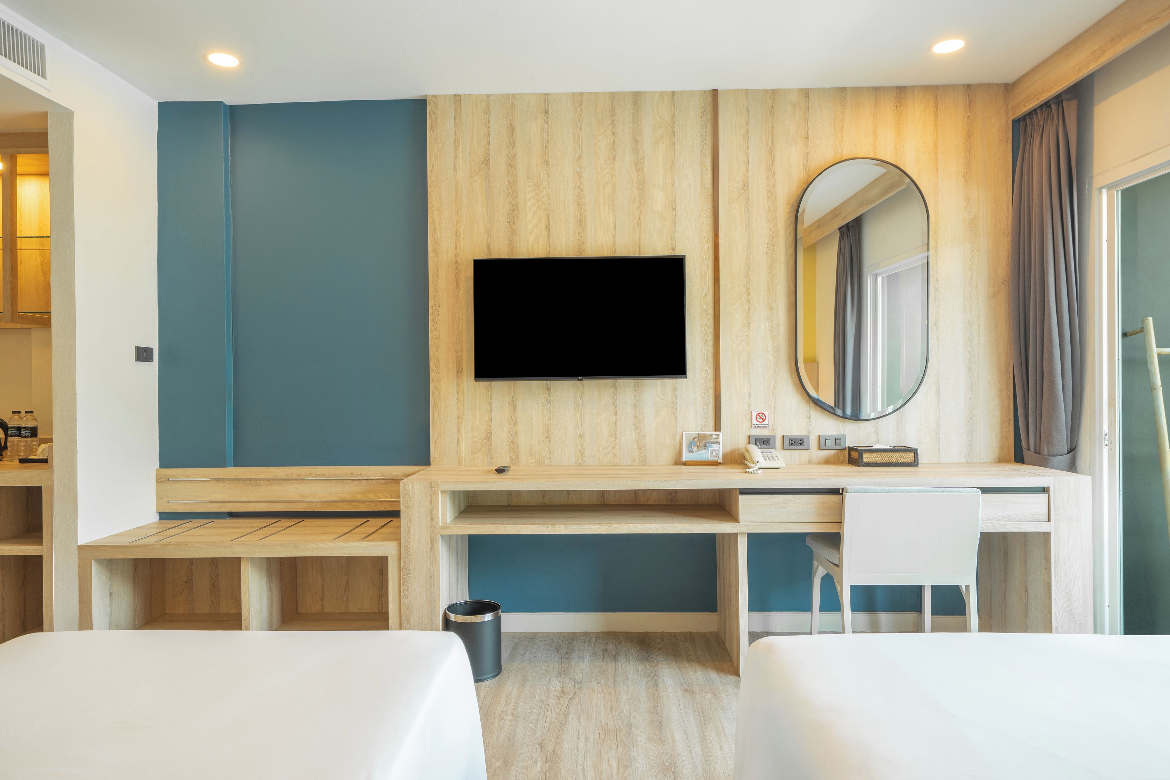 A hotel room with a bed, a desk with a chair, a television, a mirror, and a trash bin.