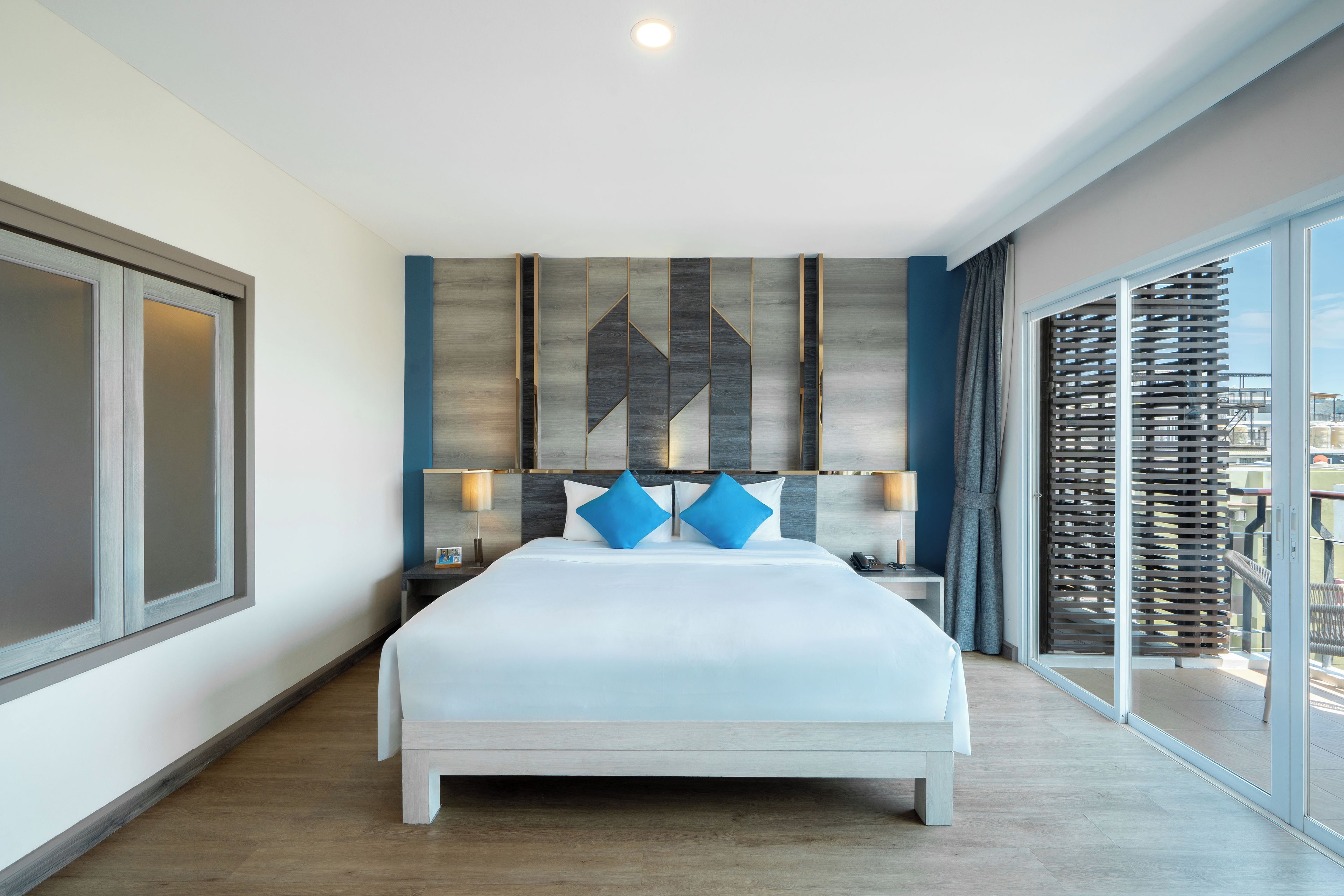 Una habitación de hotel moderna con una cama grande, una mesita de noche, una lámpara y vistas a la ciudad por la ventana.
