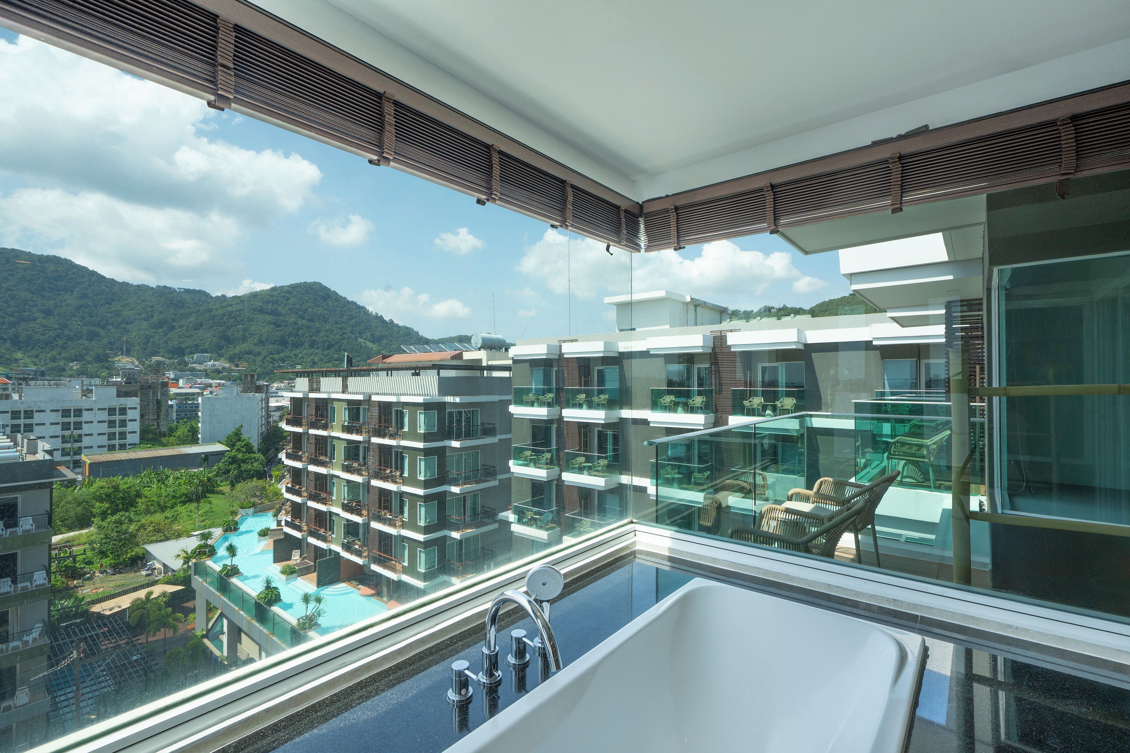 Un hotel moderno con piscina en la azotea, barandillas de cristal y vistas a la ciudad y montañas circundantes.