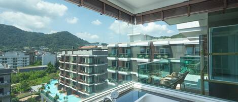 Un hotel moderno con piscina en la azotea, barandillas de cristal y vistas a la ciudad y montañas circundantes.