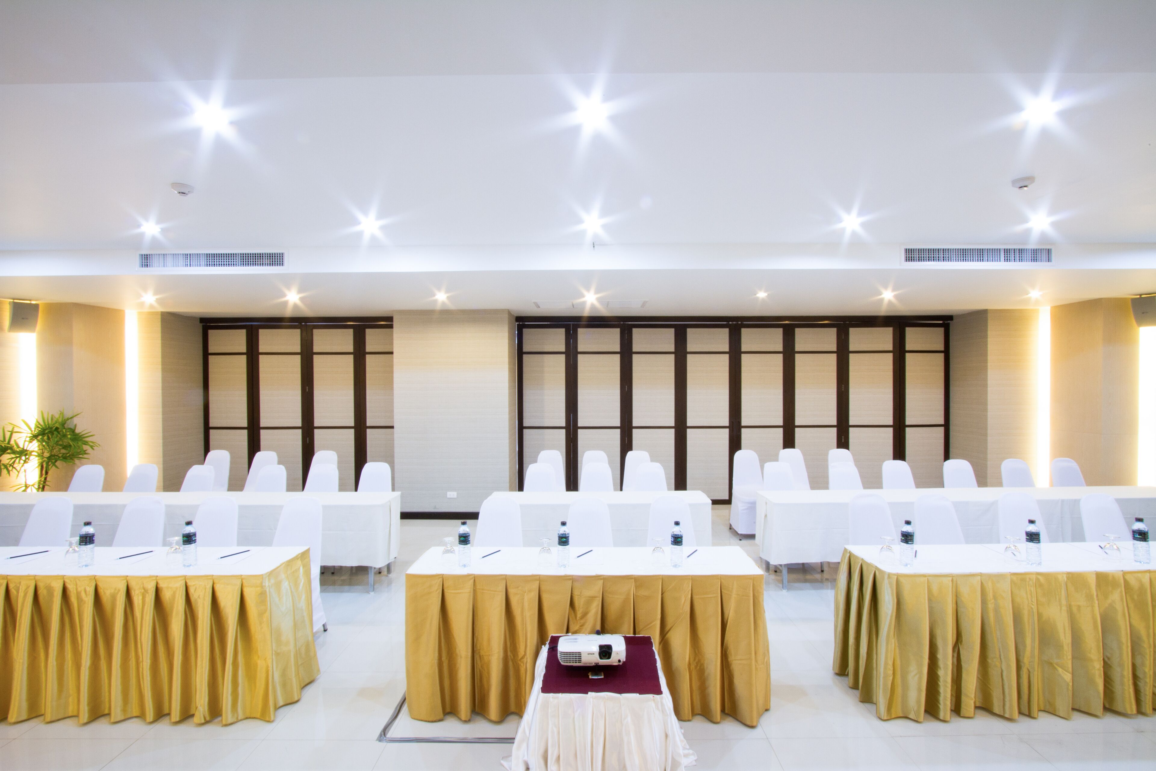 A conference room with white chairs, tables with gold tablecloths, and a projector on a table.