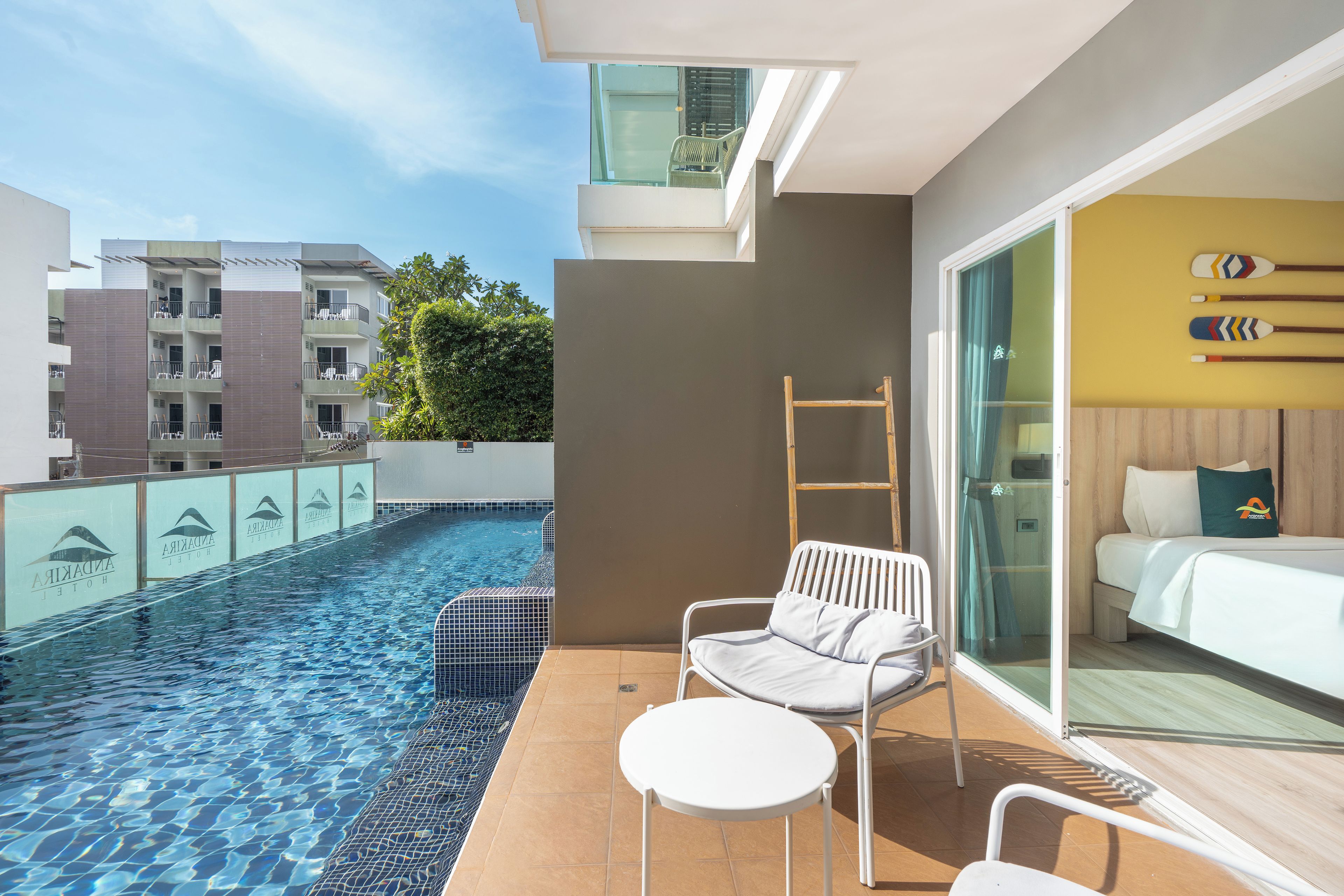 A modern hotel room with a balcony, a pool, and a view of other buildings.