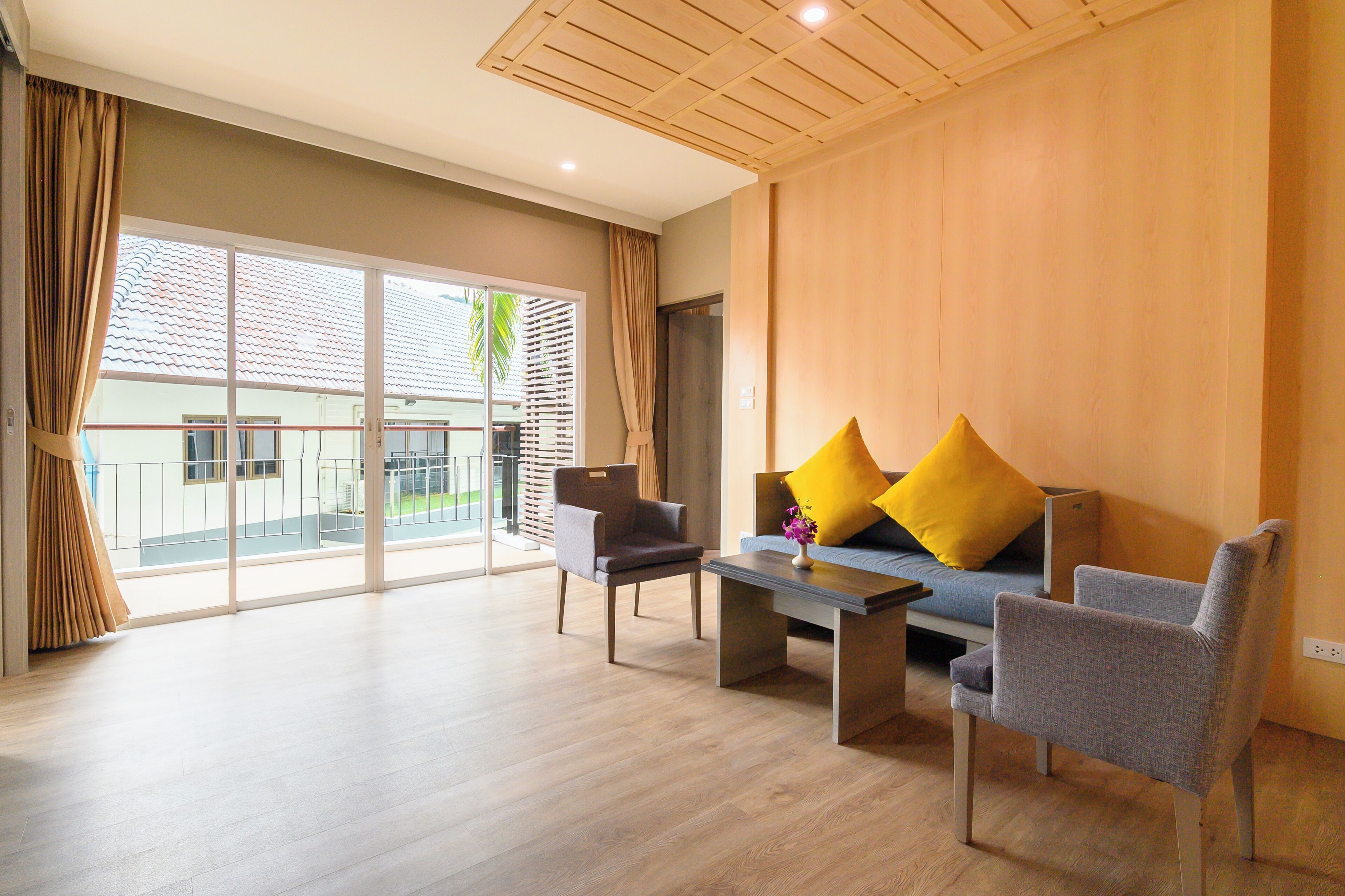 A spacious living area with a sofa, two armchairs, a coffee table, and a view of a balcony with a railing.