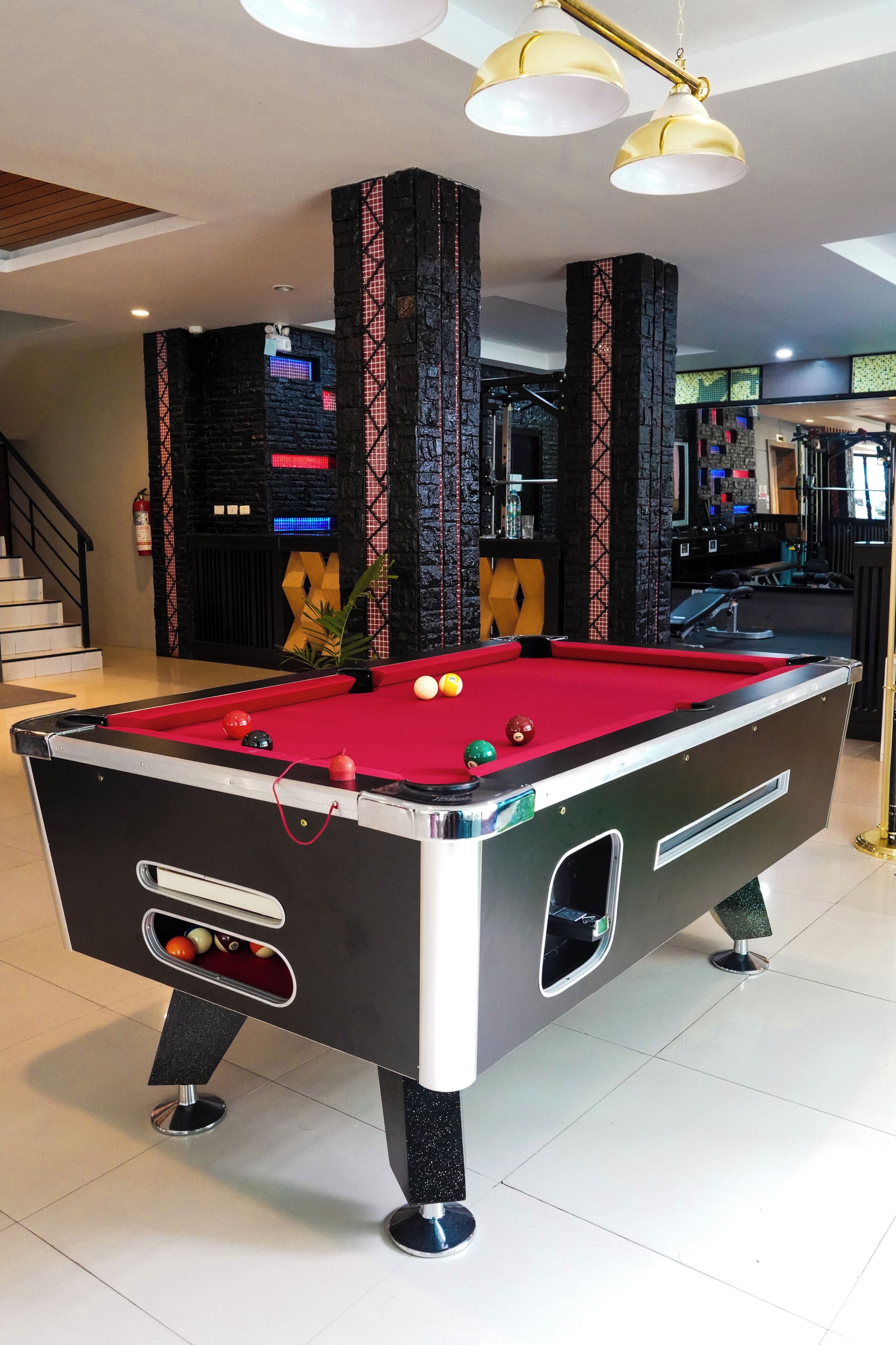 Une table de billard avec des billes, un escalier et un coin bar à l’arrière-plan.