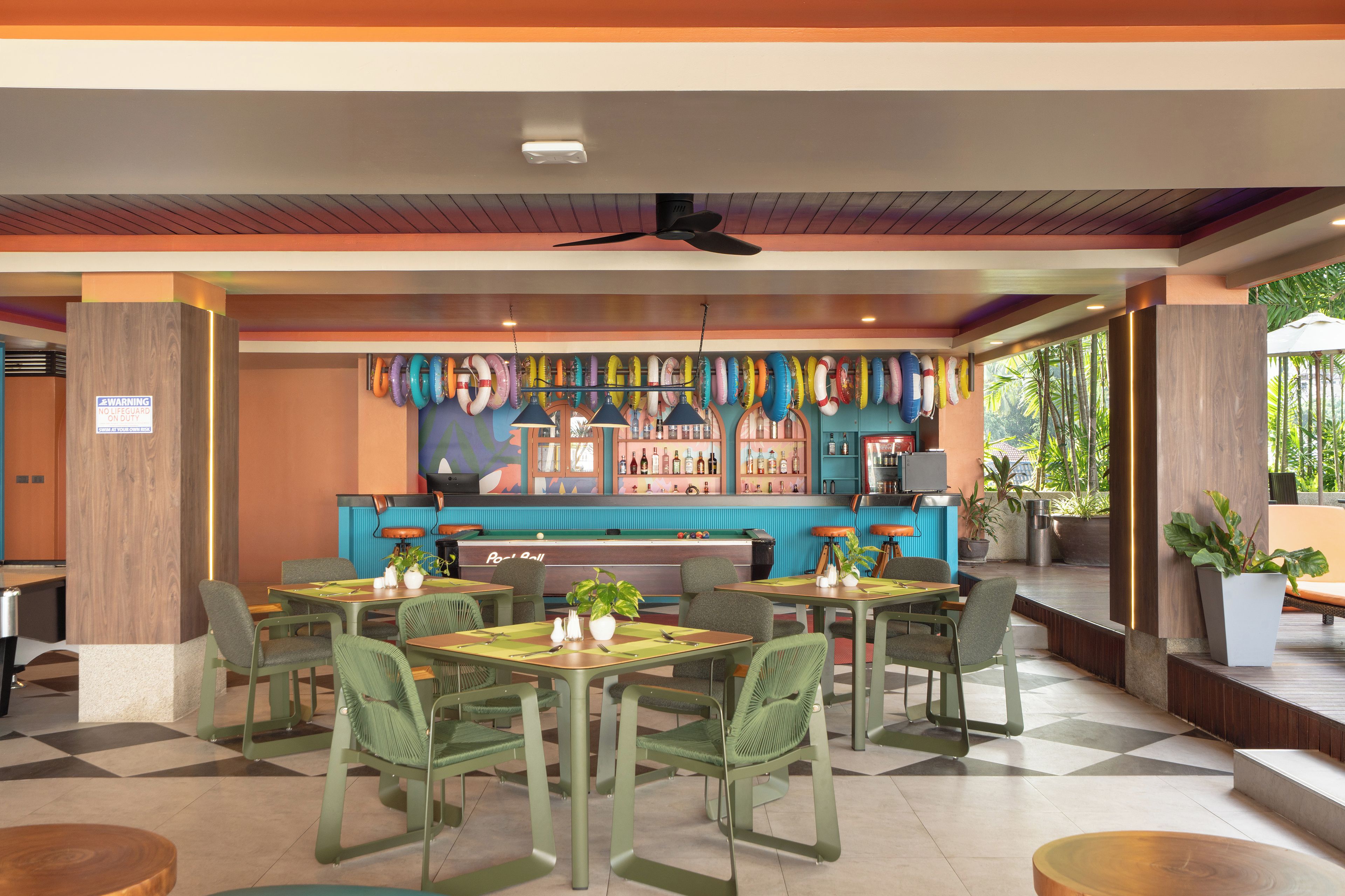 Un restaurant doté d’une table de billard, de chaises vertes et d’un bar agrémenté de décorations colorées.