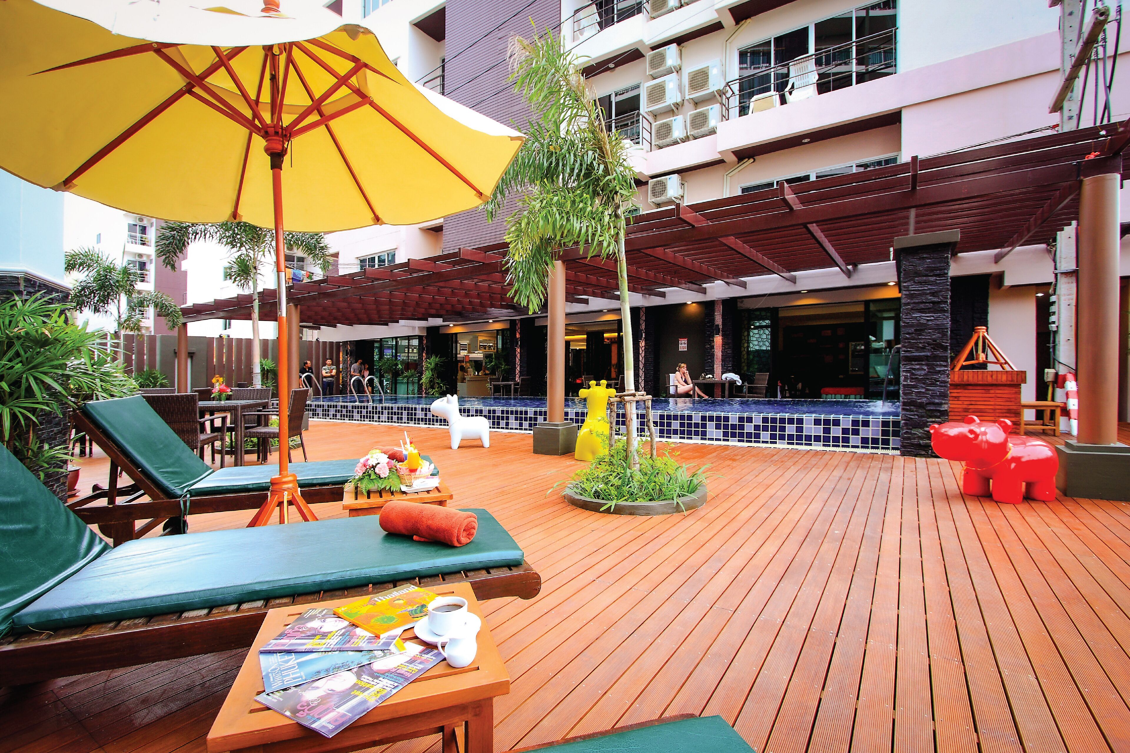 Une terrasse en bois avec des chaises longues, une table avec des magazines et un parasol jaune.