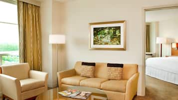 A hotel room with a sofa, armchair, and a glass coffee table.
