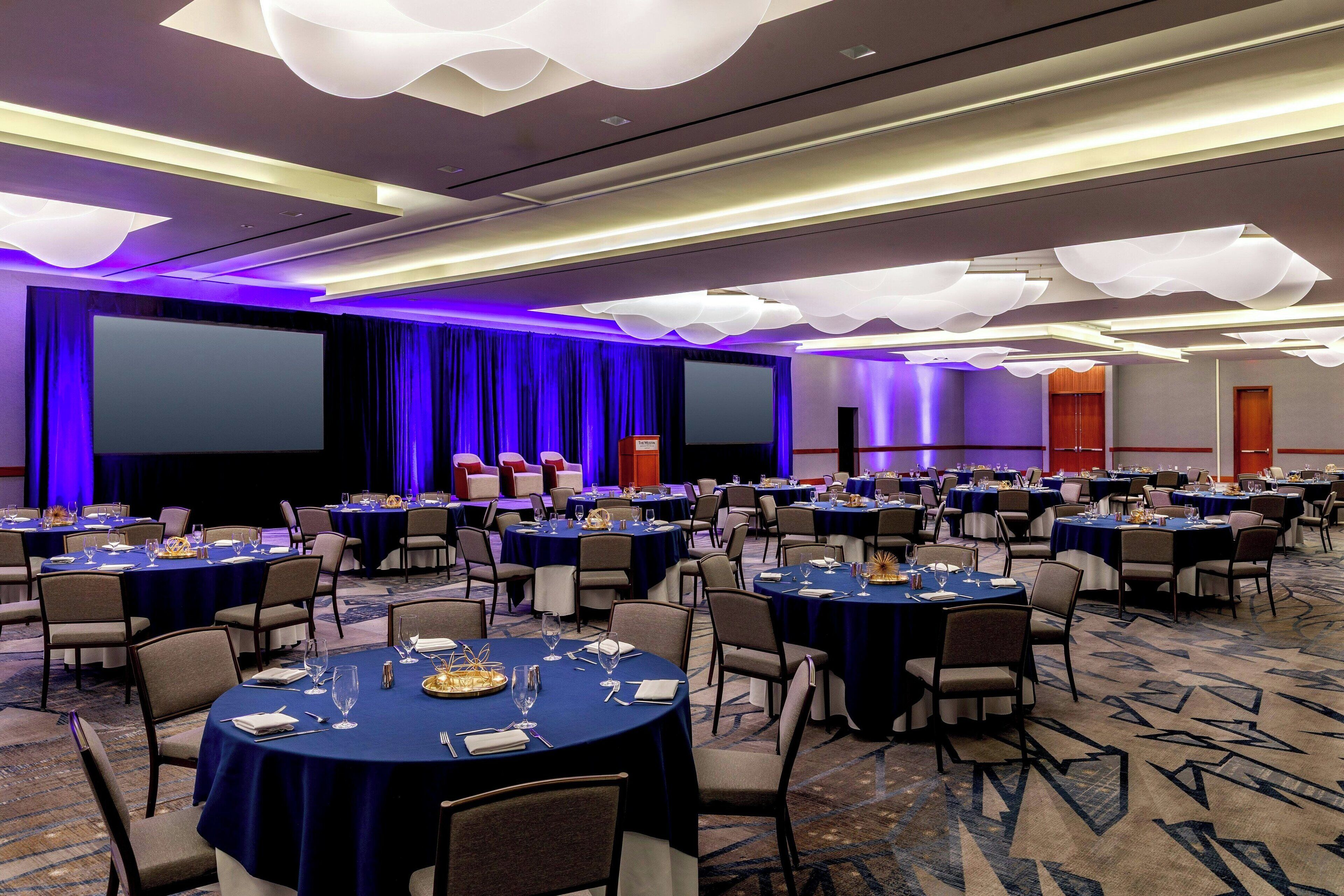 A conference room with multiple round tables, chairs, and a large screen.