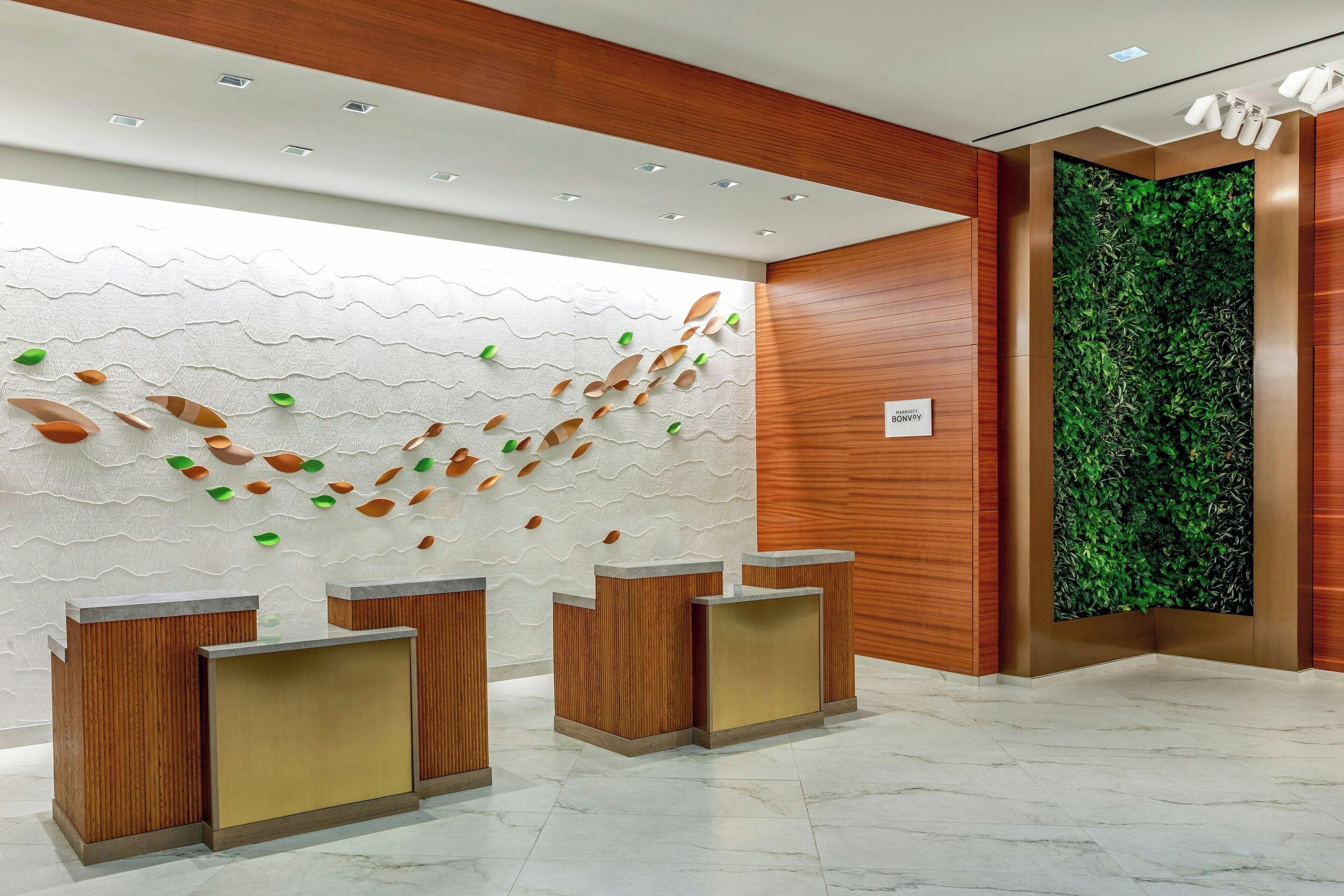 Una zona de recepción con mostradores de madera, una pared blanca con textura y decoraciones de hojas, y un jardín vertical verde.