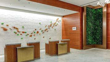 Una zona de recepción con mostradores de madera, una pared blanca con textura y decoraciones de hojas, y un jardín vertical verde.