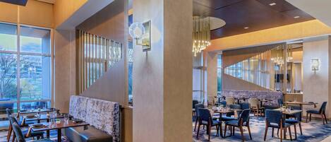 Un moderno vestíbulo de hotel con diversas zonas de estar, incluyendo un sofá y mesas de comedor.