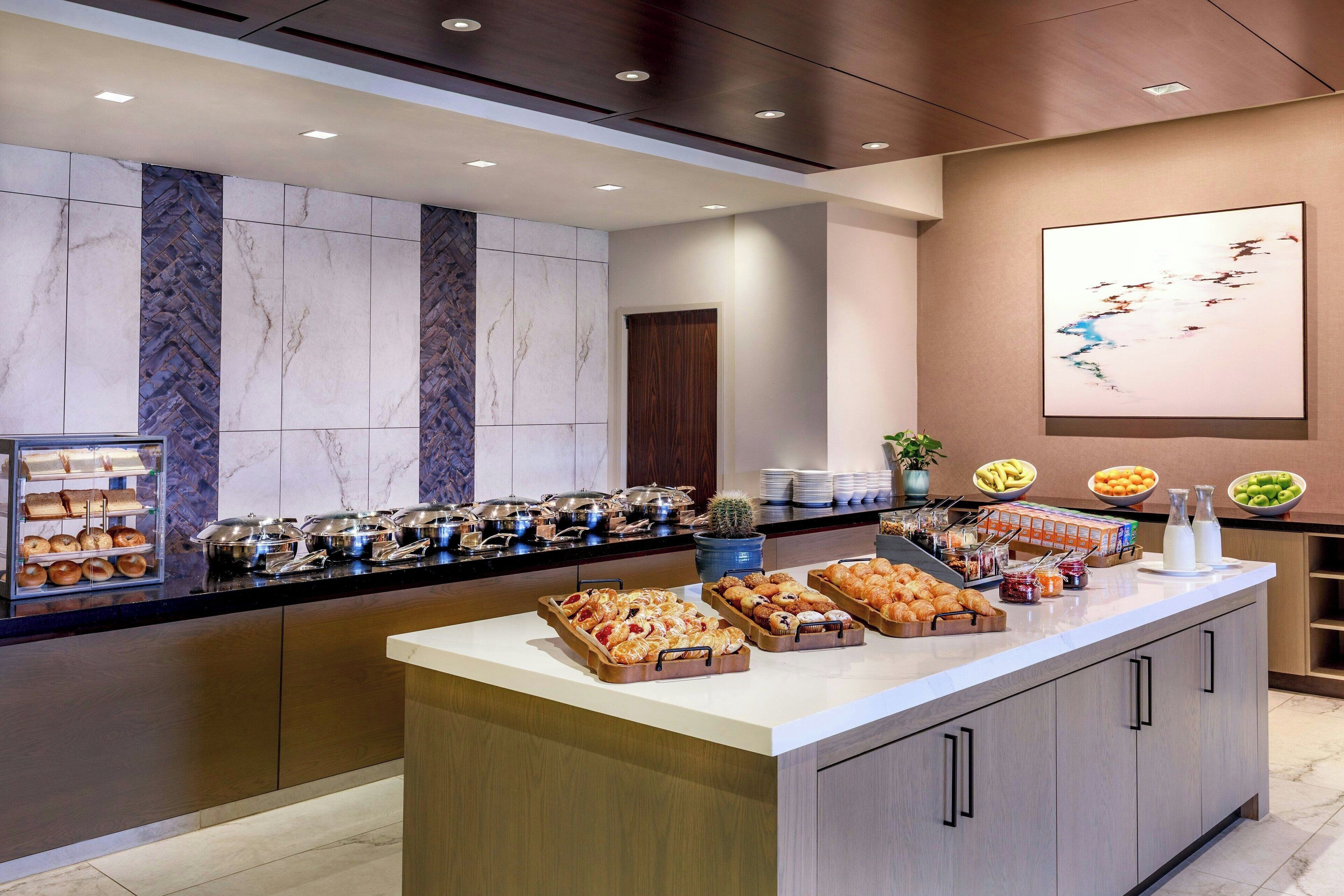A buffet counter with various food items, a potted plant, and a large abstract painting on the wall.