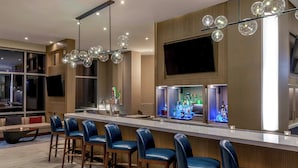 Un área de bar moderna con una barra alargada, varios taburetes y una lámpara decorativa.