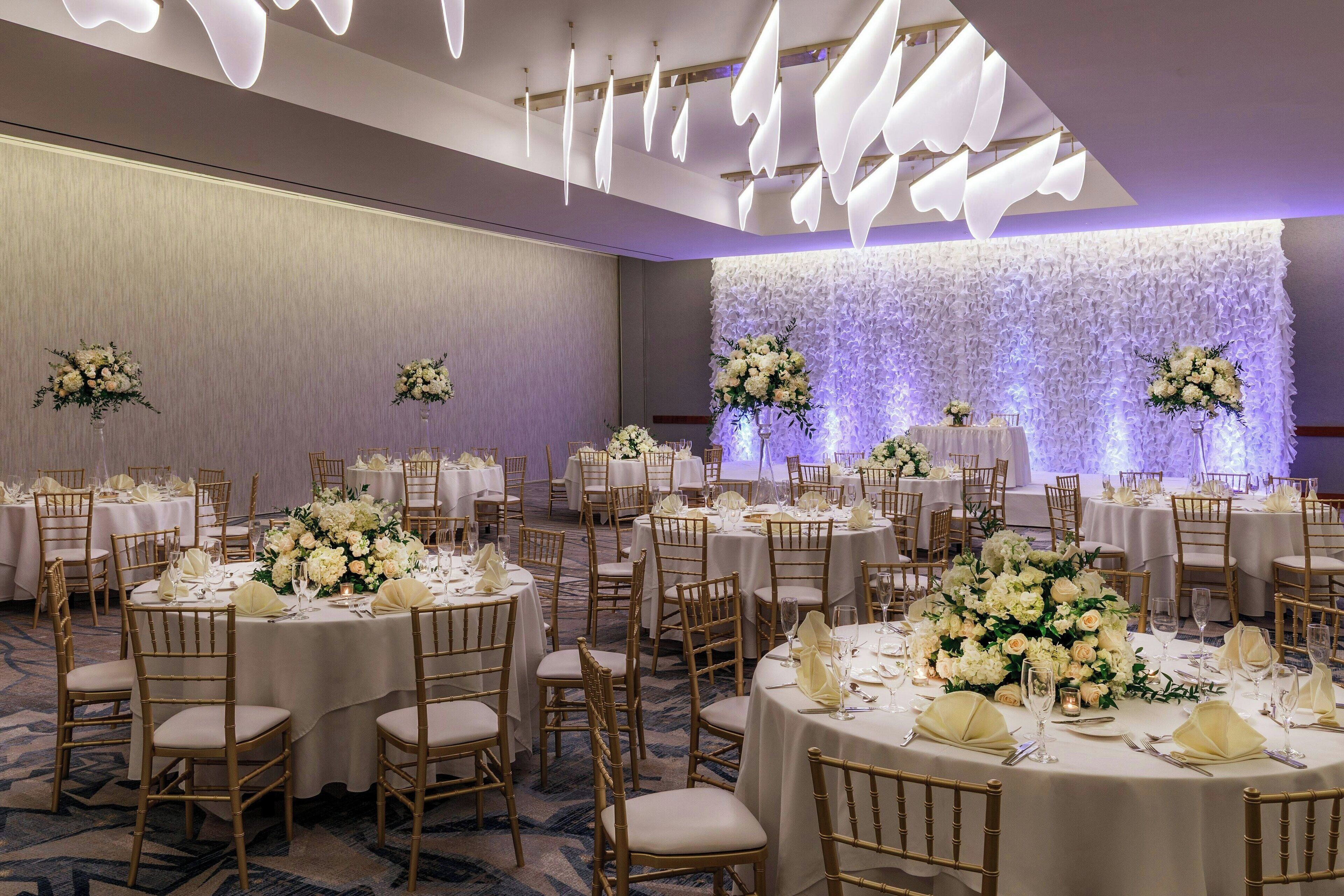 A banquet hall with round tables, gold chairs, and floral centerpieces.
