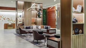 Un área de descanso moderna con un sofá modular, sillones y una mesa de centro. Hay estanterías con objetos decorativos y una pared verde decorativa.