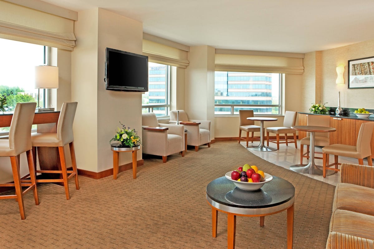 A hotel room with a seating area, a flat-screen TV mounted on the wall, and a fruit bowl on a small table.