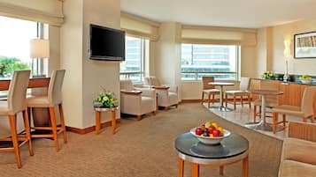 A hotel room with a seating area, a flat-screen TV mounted on the wall, and a fruit bowl on a small table.