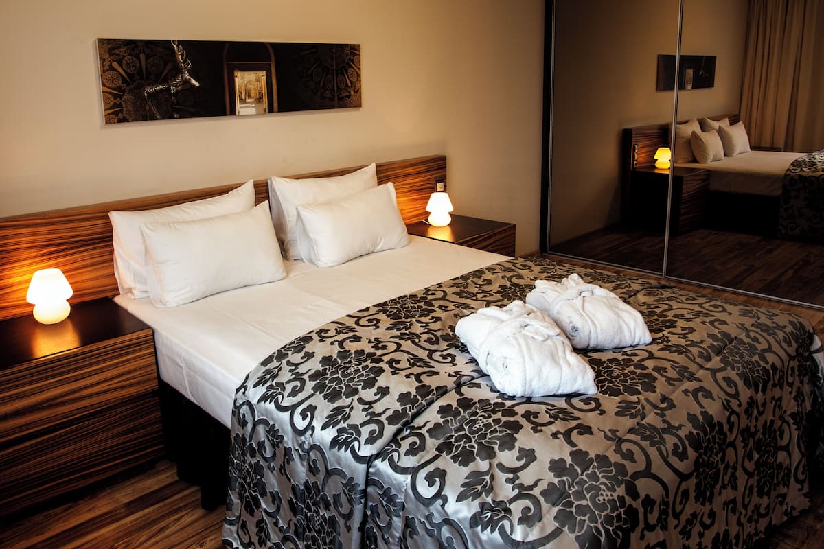 A hotel room with a large bed, two bedside tables with lamps, a mirror, and a patterned bedspread.