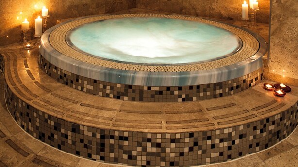 A circular hot tub with mosaic tiles and candles, surrounded by stone walls and recessed lighting. - Ararat All Suites Hotel (Klaipeda)