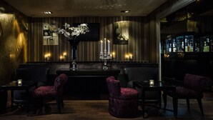 A dimly lit bar area with a piano, two velvet chairs, a candelabra, and a large mirror reflecting the bar. - Ararat All Suites Hotel (Klaipeda)