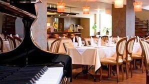 A restaurant with a grand piano, wooden tables, and chairs. - Ararat All Suites Hotel (Klaipeda)