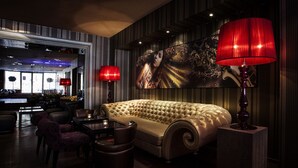 A luxurious lounge area with a tufted sofa, a bar in the background, and two red lamps. - Ararat All Suites Hotel (Klaipeda)