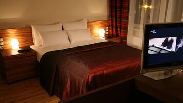 Una camera d'albergo con un letto, due lampade ai comodini, una televisione e una finestra con tende.