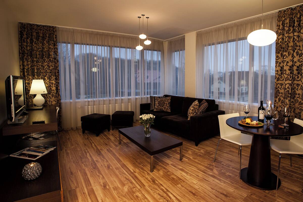 A modern living room with a dark sofa, a coffee table, and a dining table with a candle and wine.