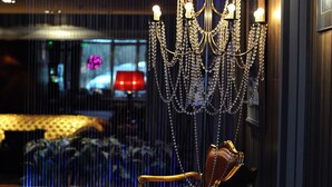 A luxurious room with a classic wooden chair, a decorative chandelier, and a view through a window with blinds. - Ararat All Suites Hotel (Klaipeda)
