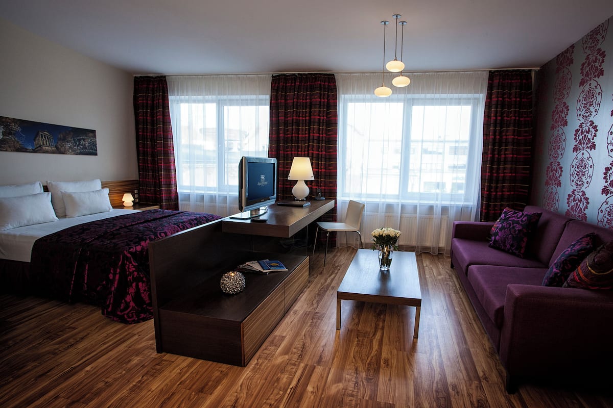 A hotel room with a bed, a desk with a computer, a coffee table, a sofa, and a TV.