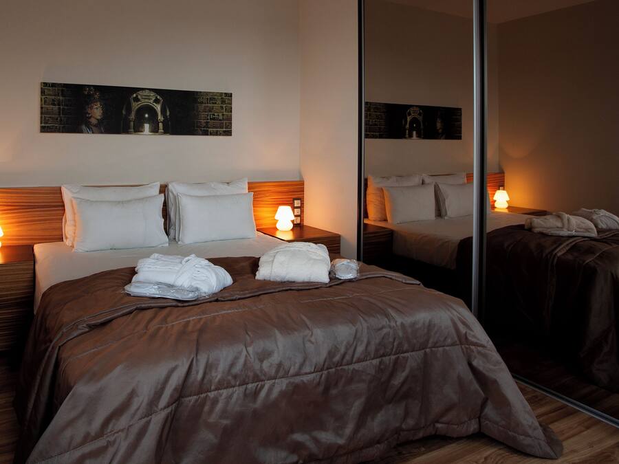 Een hotelkamer met een groot bed, twee nachtkastjes met lampen, een spiegel en kunst aan de muur.
