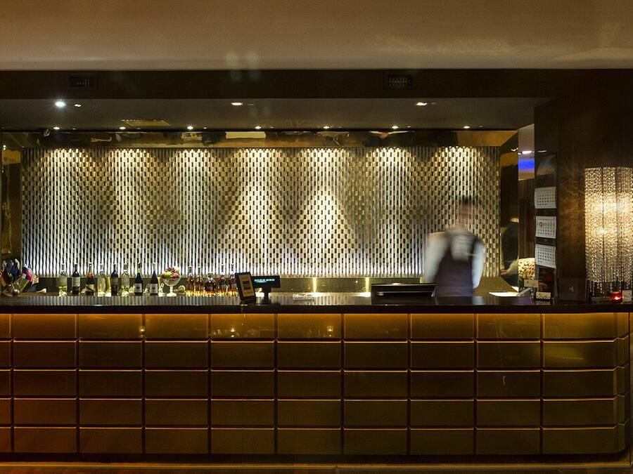 Een bar met een toonbank, planken vol flessen en een behang met patroon.
