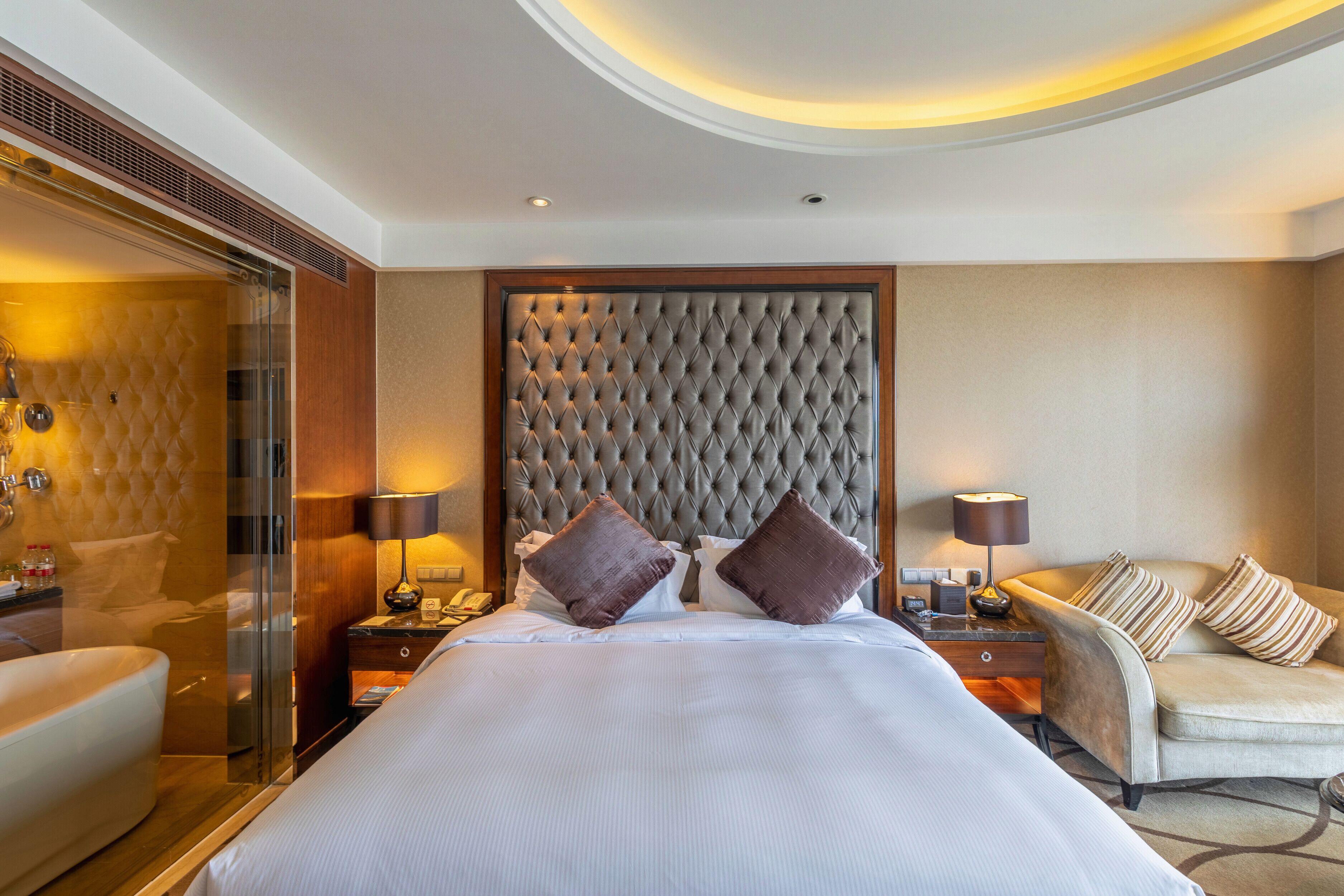 Une chambre d’hôtel dotée d’un grand lit, d’un coin salon avec un canapé, d’une douche en verre et d’une tête de lit en bois.