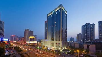 A high-rise building with a modern glass facade, surrounded by a busy urban street at dusk.
