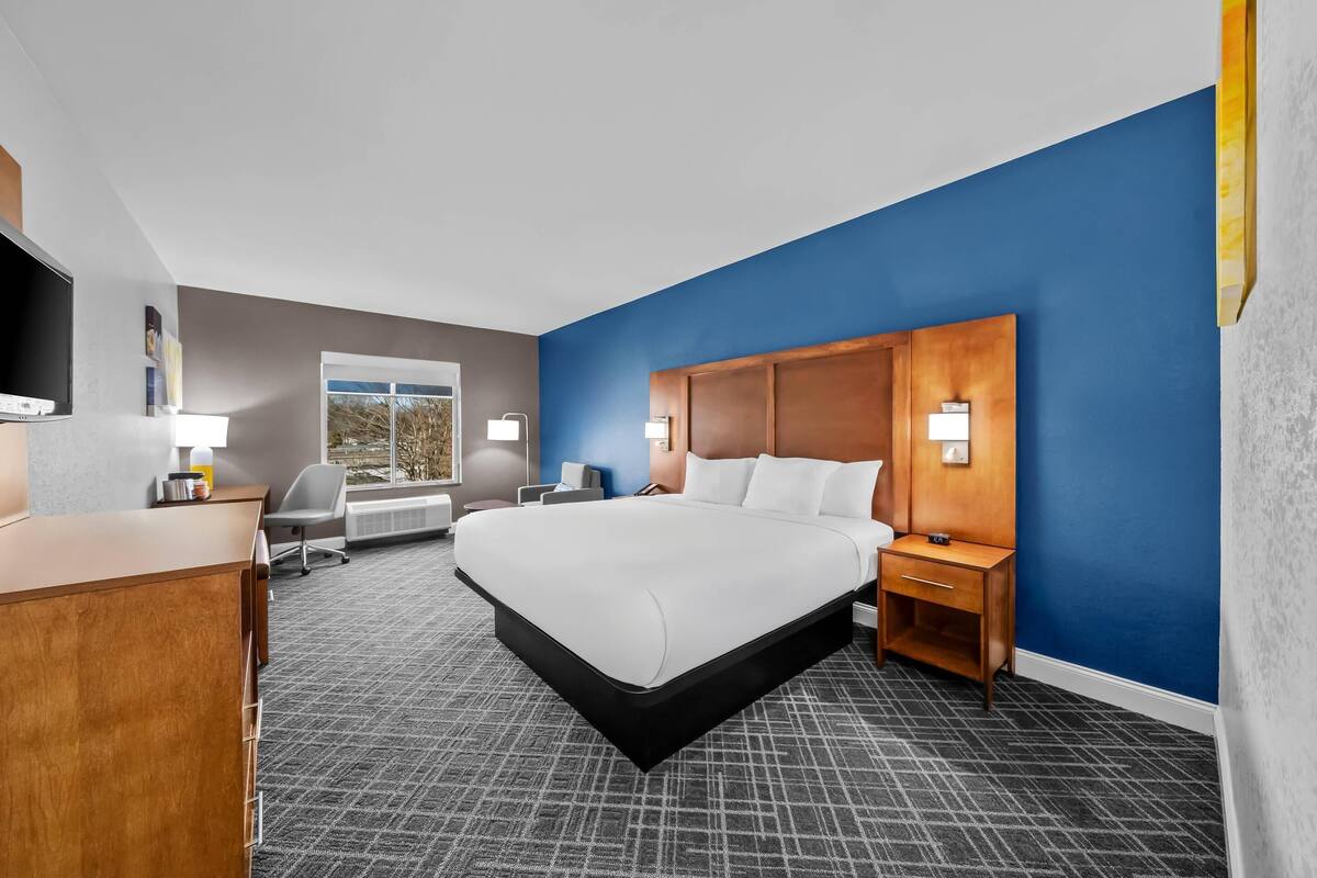 A hotel room with a large bed, a desk, a chair, and a television.