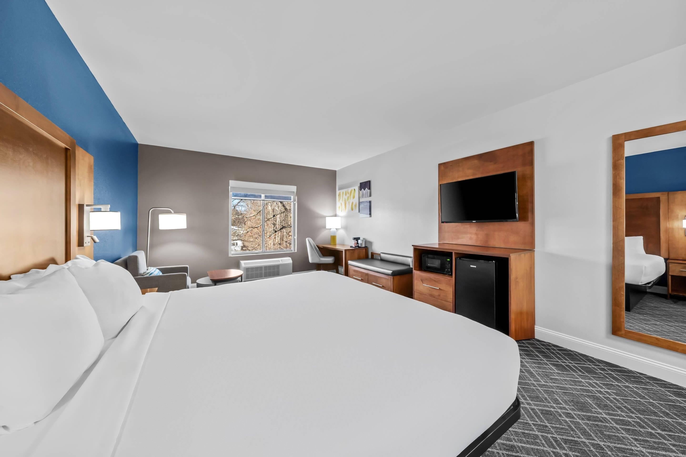 A hotel room with a large bed, a desk, a chair, a TV, and a mirror.