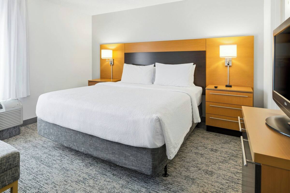 A hotel room with a large bed, bedside tables with lamps, a desk with a computer, and a TV.