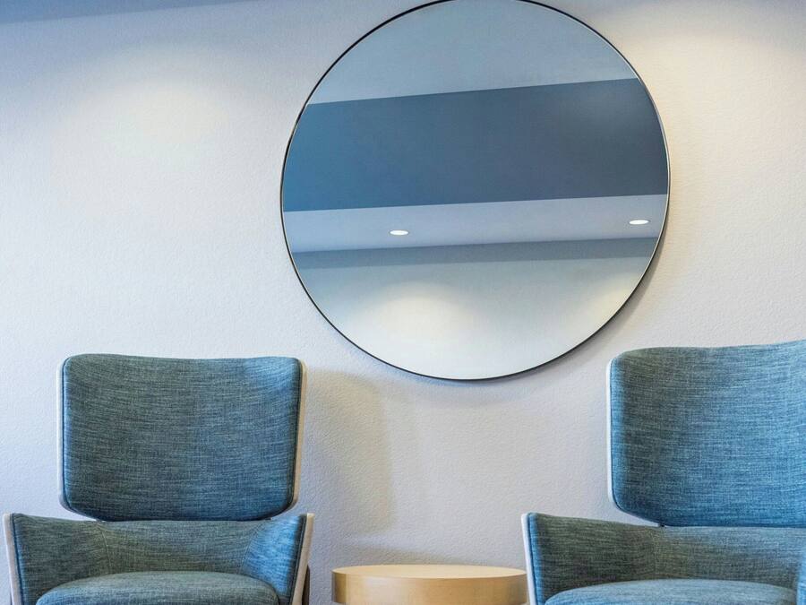 Een kamer met twee stoelen, een ronde spiegel en een klein tafeltje.