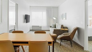 A hotel room with a wooden table, two chairs, a sofa, a TV, and a lamp. - TownePlace Suites by Marriott Farmington (Farmington)