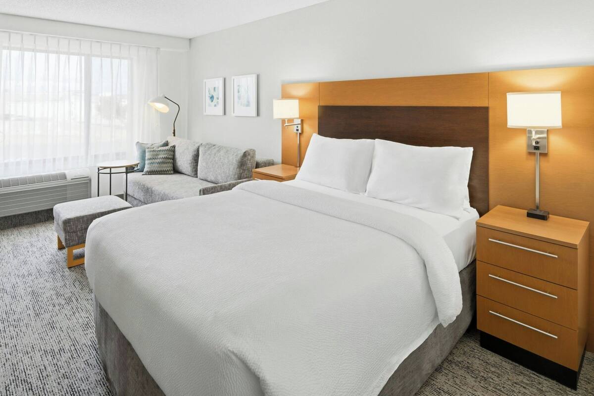 A hotel room with a large bed, two bedside tables, a sofa, a lamp, and a window with curtains.