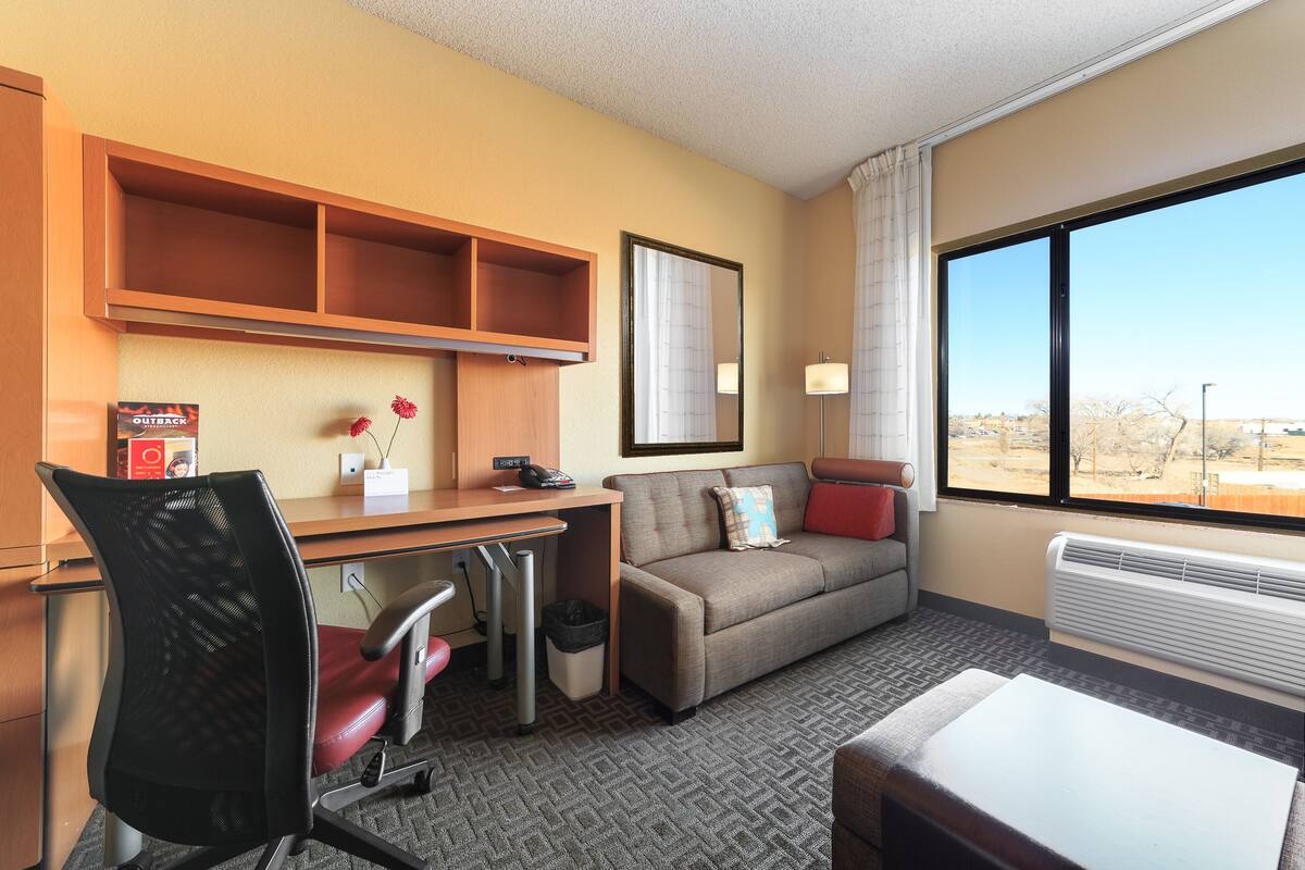 A hotel room with a desk, office chair, sofa, and a large window offering a view of the outdoors.