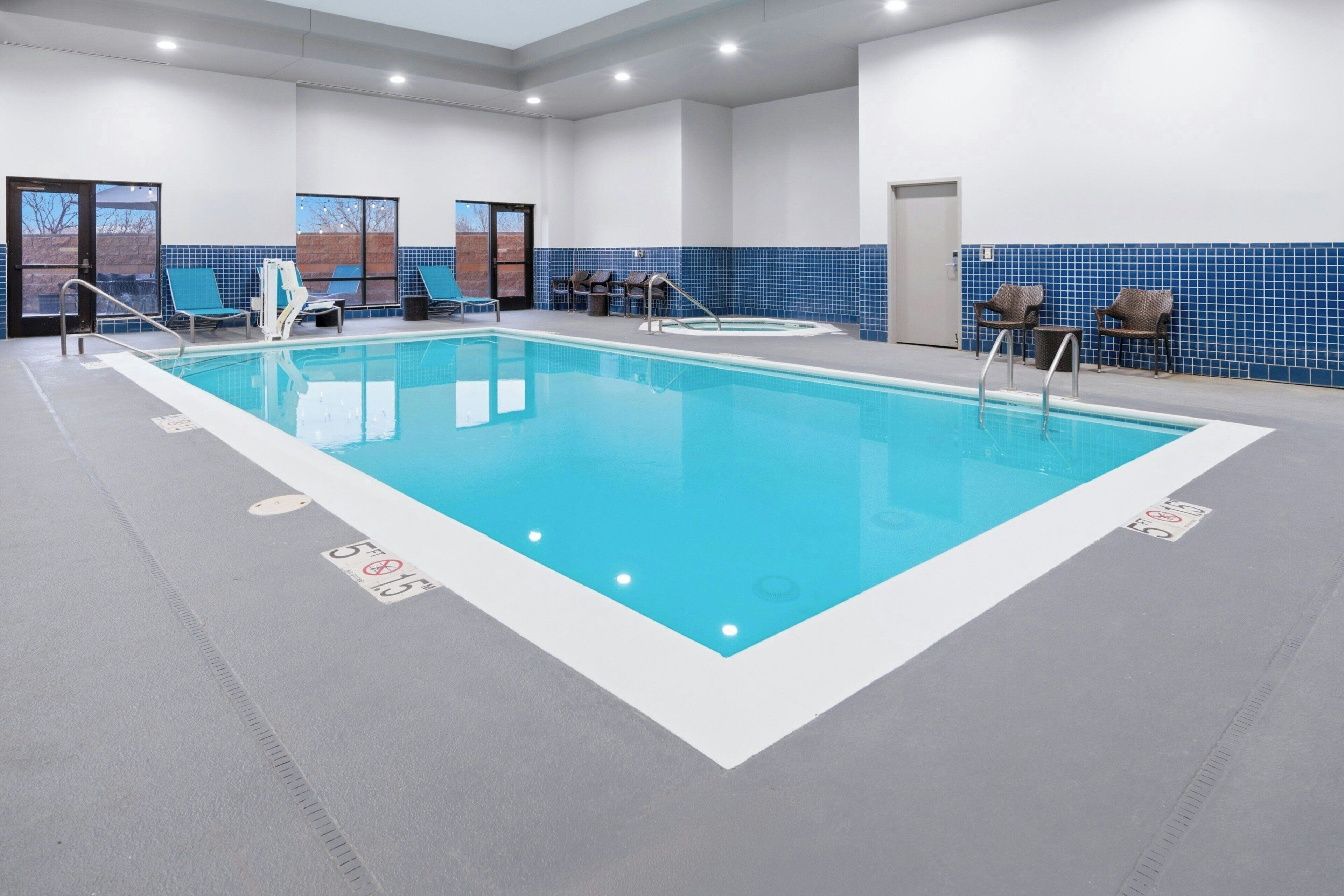 An indoor swimming pool with clear blue water, a tiled blue wall, and several lounge chairs.