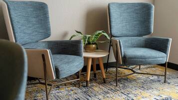 Deux fauteuils bleus, une petite table ronde ornée d’une plante et un tapis à motifs dans une pièce aux murs unis.
