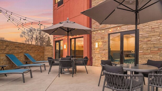 An outdoor patio with lounge chairs, a round table, and umbrellas. - TownePlace Suites by Marriott Farmington (Farmington)