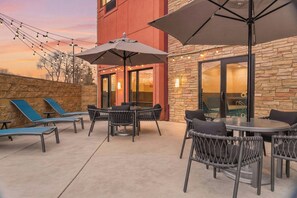 An outdoor patio with lounge chairs, a round table, and umbrellas. - TownePlace Suites by Marriott Farmington (Farmington)