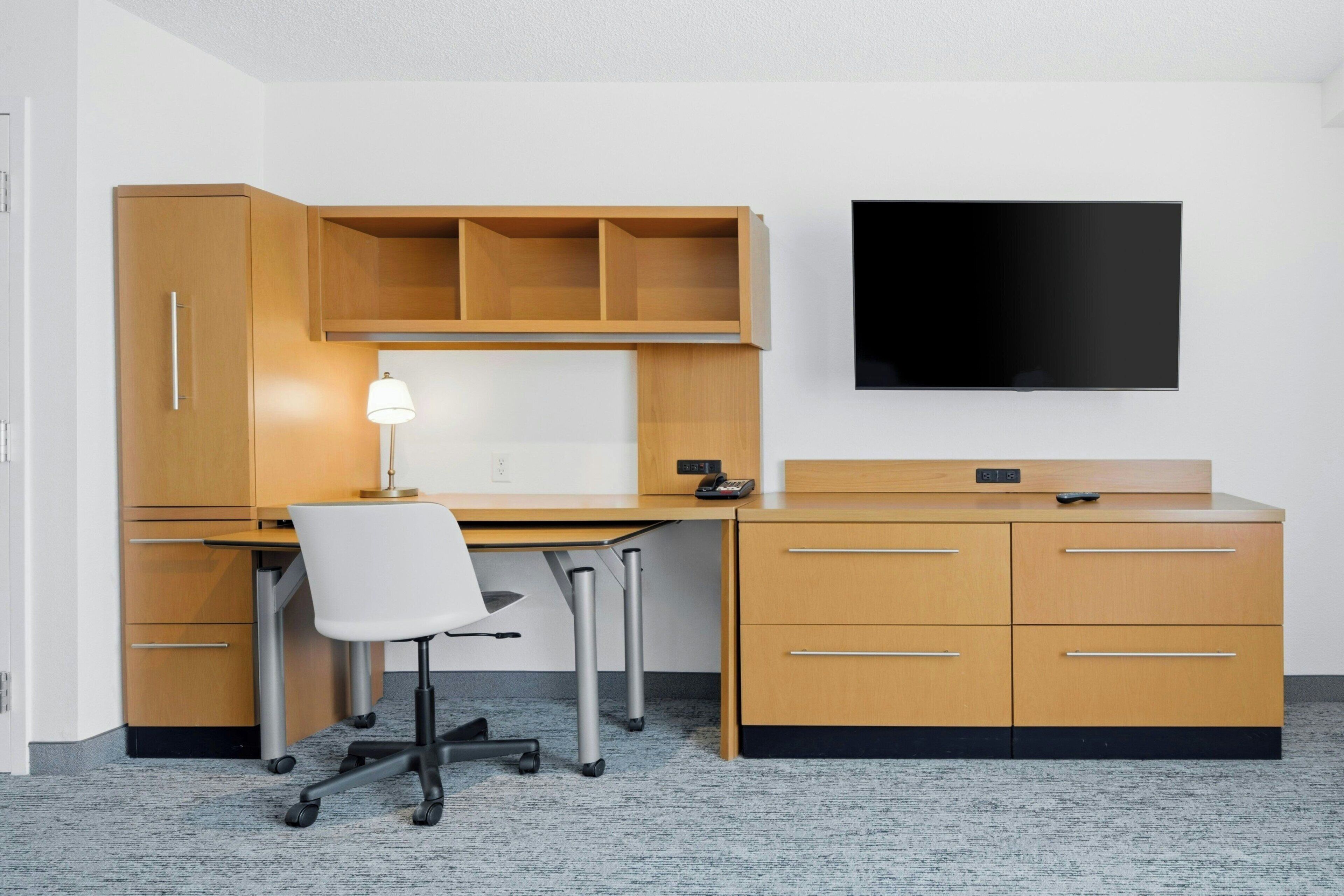 Ein moderner Arbeitsraum mit Schreibtisch, Stuhl, Holzschränken und einem an der Wand befestigten Fernseher.