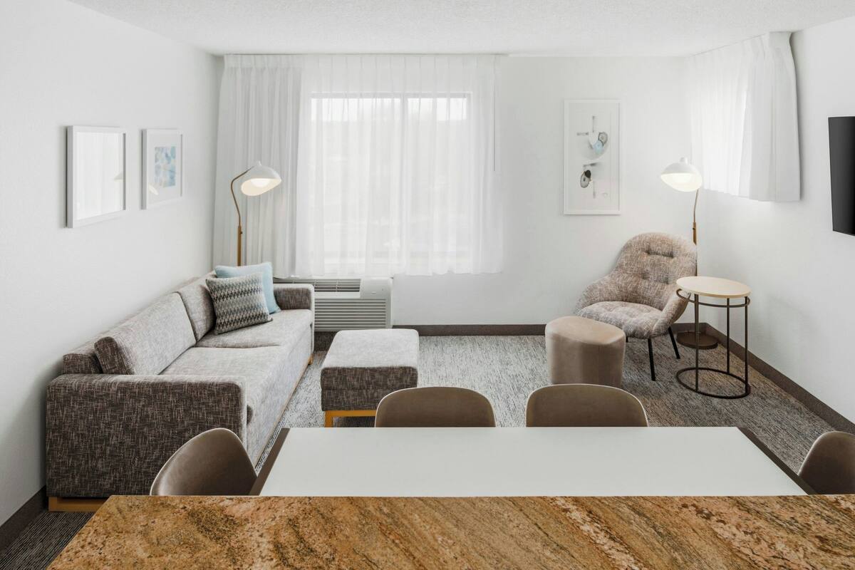 A modern living room with a sofa, ottoman, chairs, a table, and a lamp.