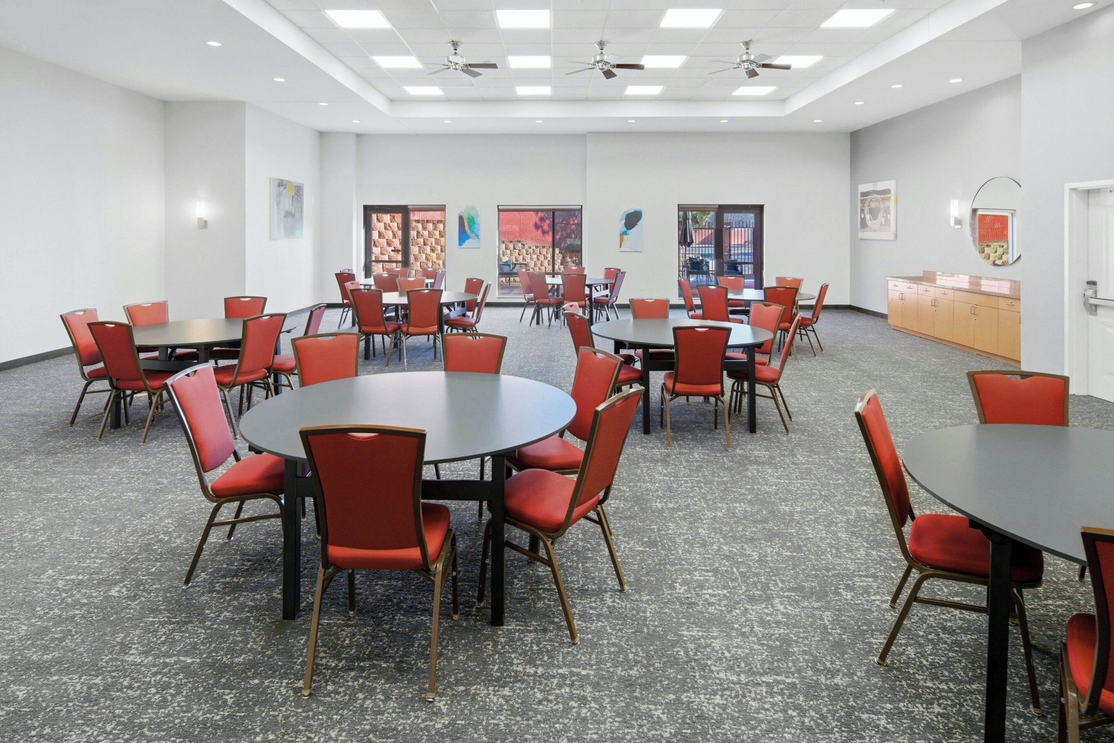 Un salón de conferencias con mesas redondas y sillas rojas, paredes blancas y ventiladores de techo.